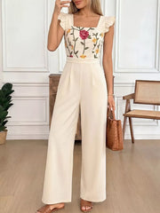 Beige floral embroidered ruffle jumpsuit with square neckline and wide legs.