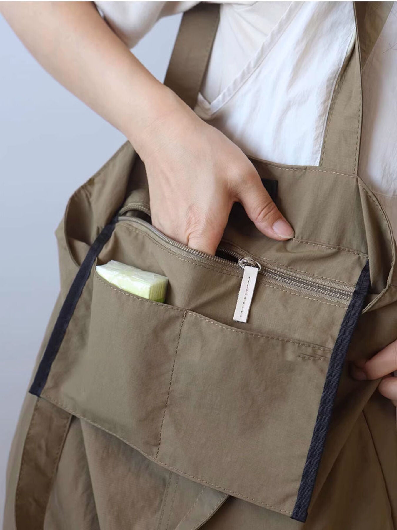 Khaki nylon shoulder bag with exterior slip pockets and zippered compartment.