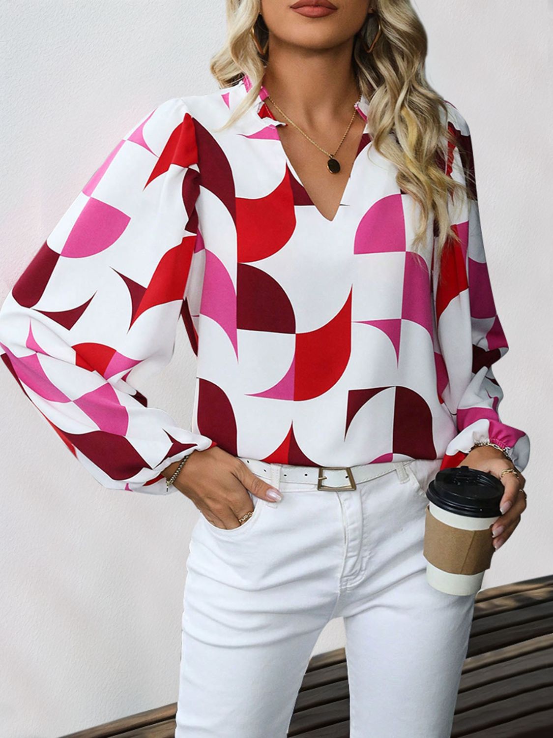 Geometric print blouse with voluminous sleeves and V-neck in white with red and pink pattern.