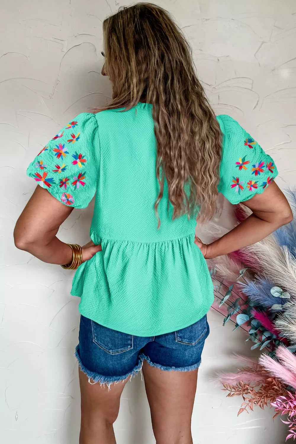 Green textured puff sleeve blouse with floral embroidery and peplum hem.