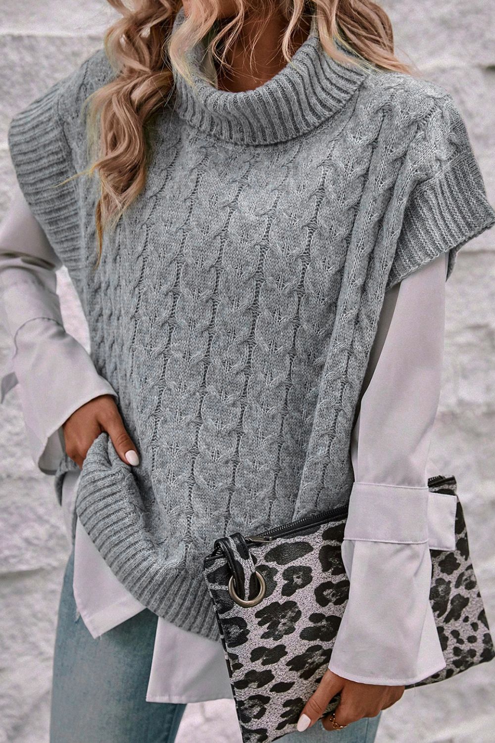 Gray cable knit turtleneck capelet sweater with short sleeves, styled with a white shirt and leopard clutch.
