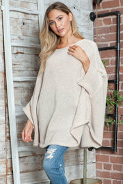 Cream knit sweater with cape sleeves and a relaxed fit, styled with ripped jeans.