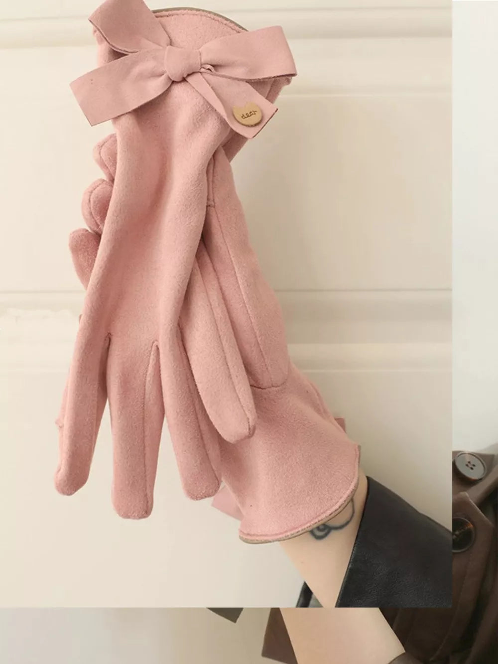 Pink suede gloves with bow detail and button accent.