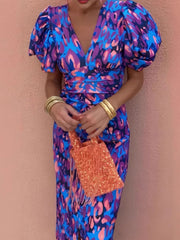 Vibrant V-neck midi dress with abstract print and puff sleeves in blue and purple, worn with gold bangles.
