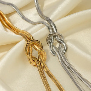 Gold and silver herringbone knot necklaces on satin fabric