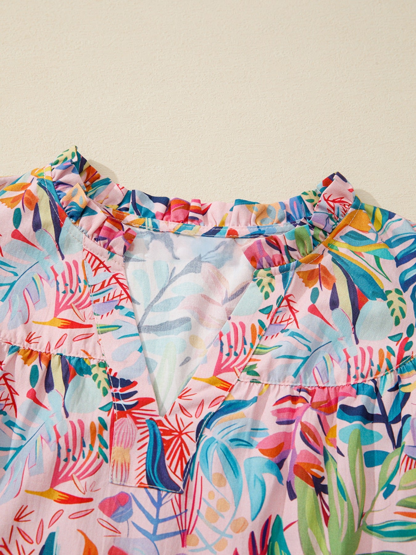 Tropical floral print cotton blouse with ruffled V-neck and short sleeves.