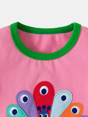 Pink cotton toddler girls' top with peacock embroidery and green trim neckline.