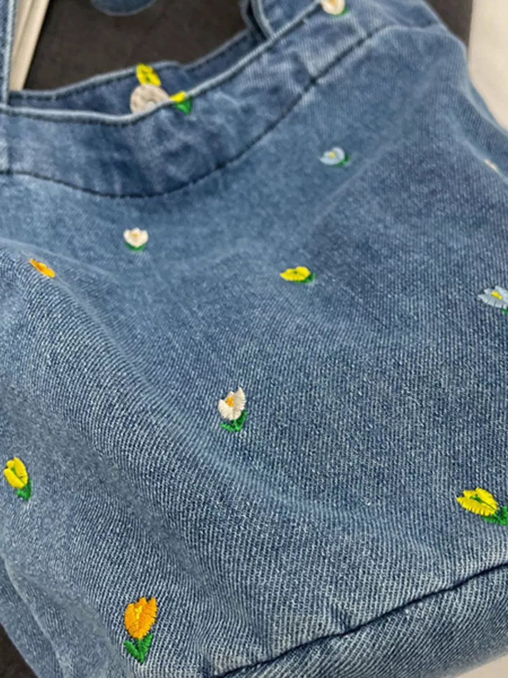 Denim tote bag with small embroidered whimsical flowers in yellow, white, and blue.