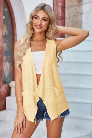 Yellow eyelet drape front vest with pockets and open front, styled with a white top and denim shorts.