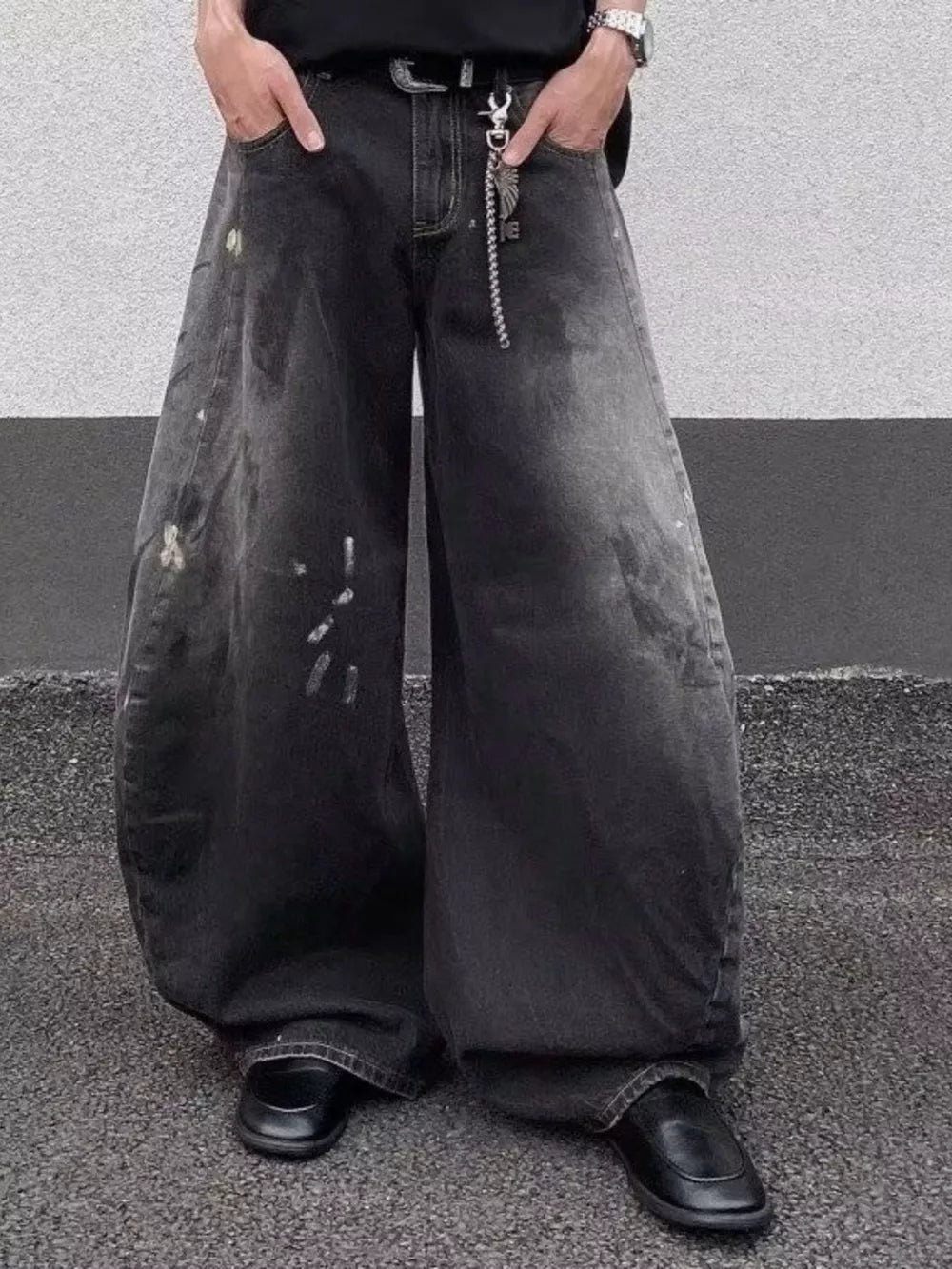 Men's black wide leg distressed jeans with paint splatters and chain detail.