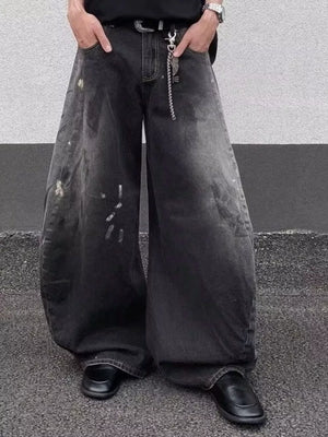 Men's black wide leg distressed jeans with paint splatters and chain detail.