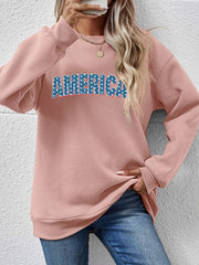 Blush pink crewneck sweatshirt with "AMERICA" graphic in blue and white stars.