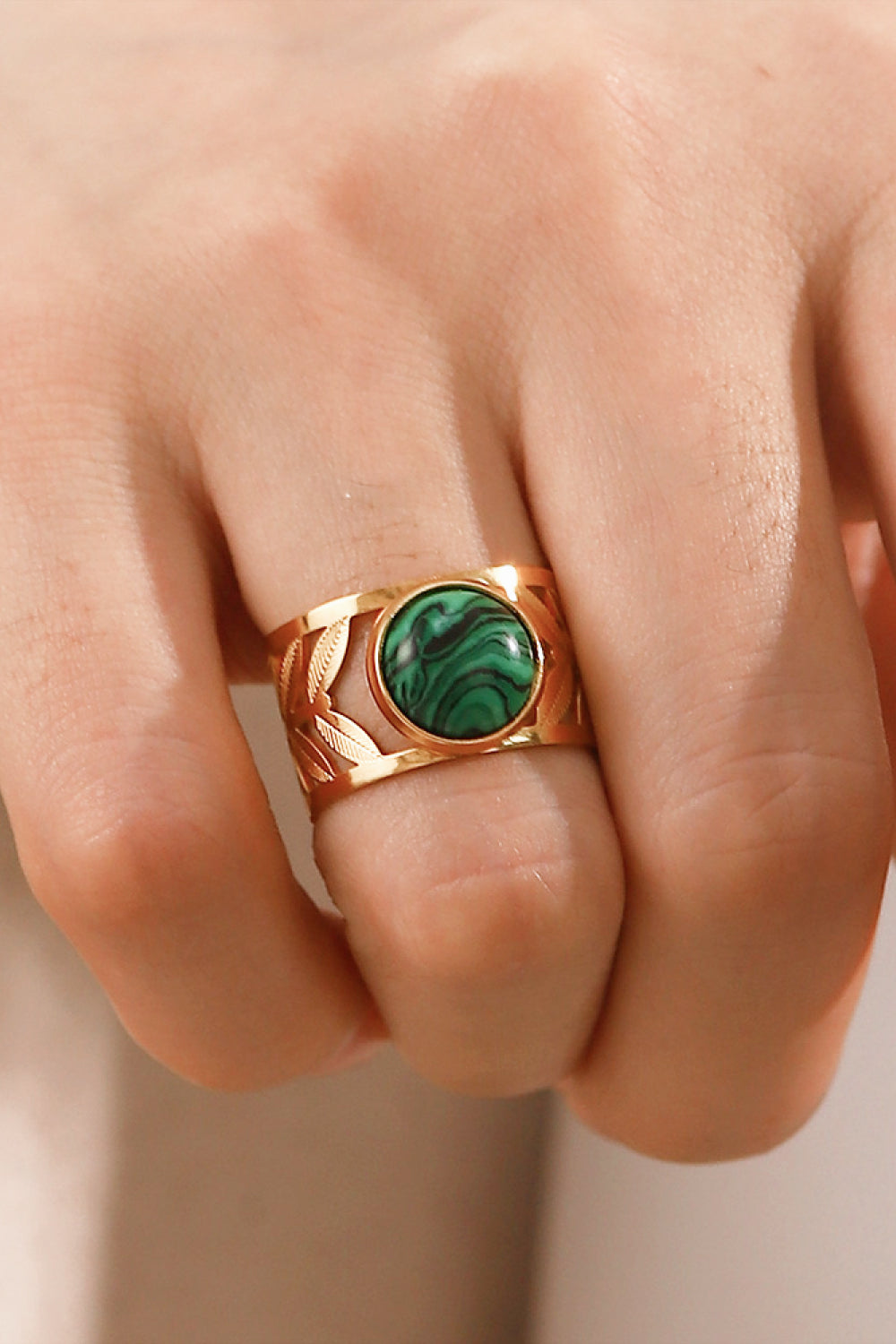 Gold ring with malachite stone and leaf cutouts on a finger