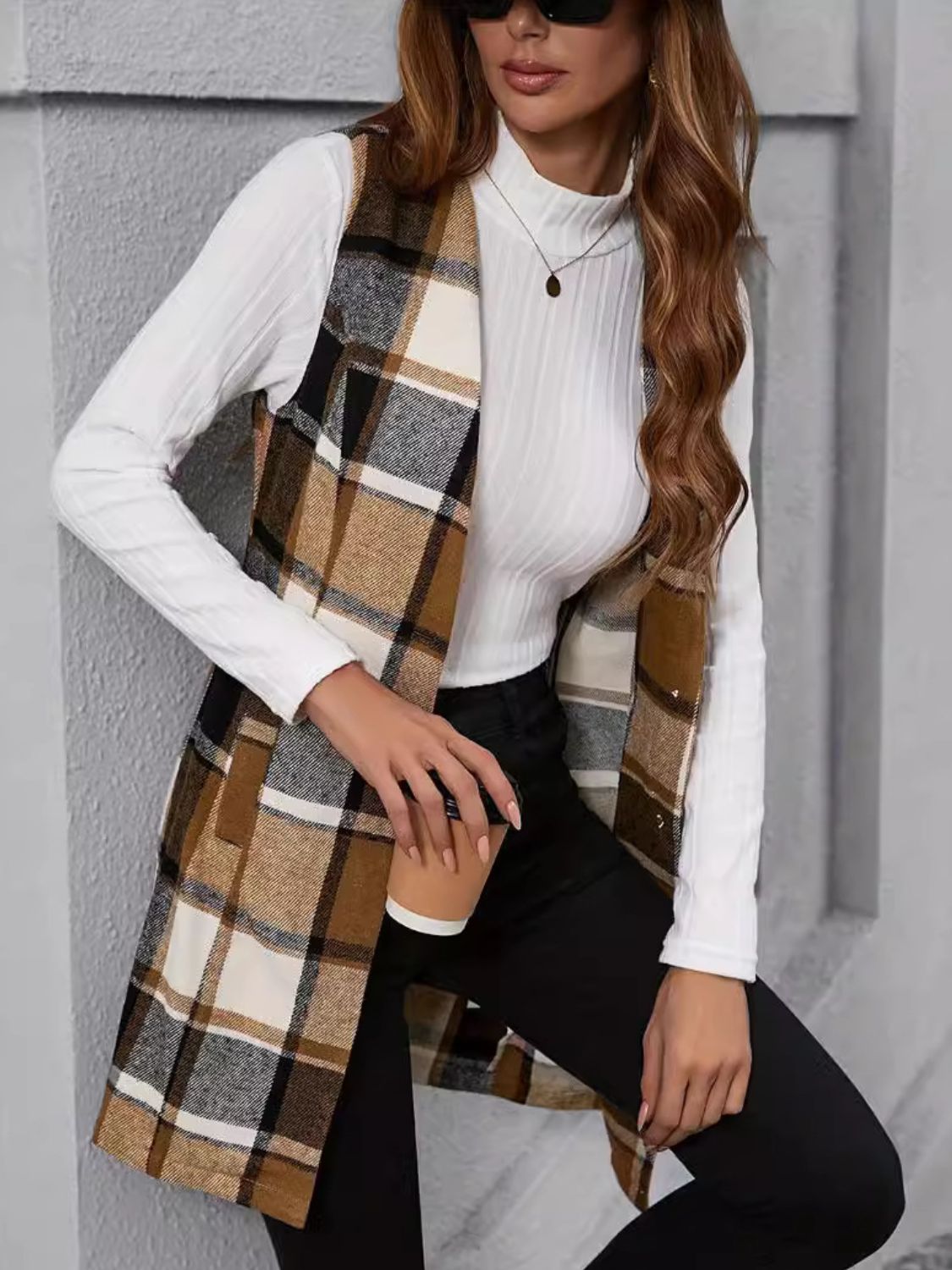 Tartan longline vest in camel with a buttoned front, worn over a white turtleneck and black pants.