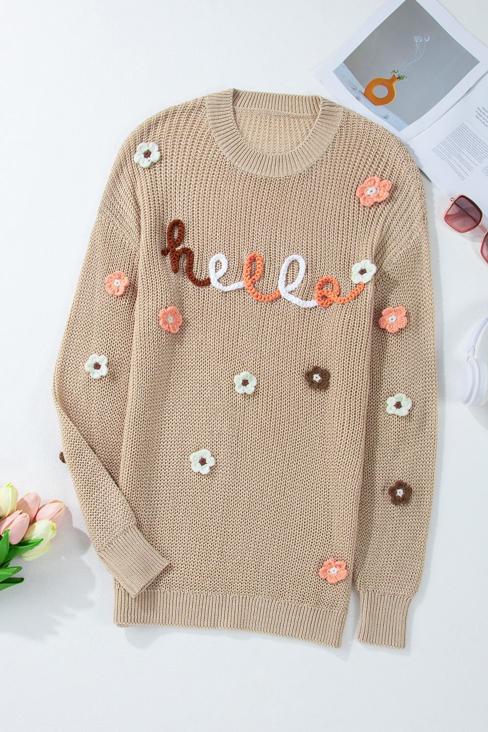 Khaki knit sweater with embroidered "hello" text and floral appliques.