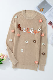 Khaki knit sweater with embroidered "hello" text and floral appliques.