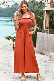 Orange smocked bodice tie-strap palazzo jumpsuit with wide legs and pockets.