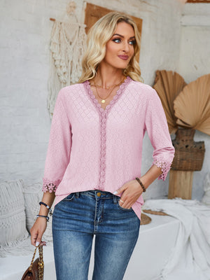 Blush pink eyelet trimmed V-neck blouse with lace detail on neckline and sleeves.