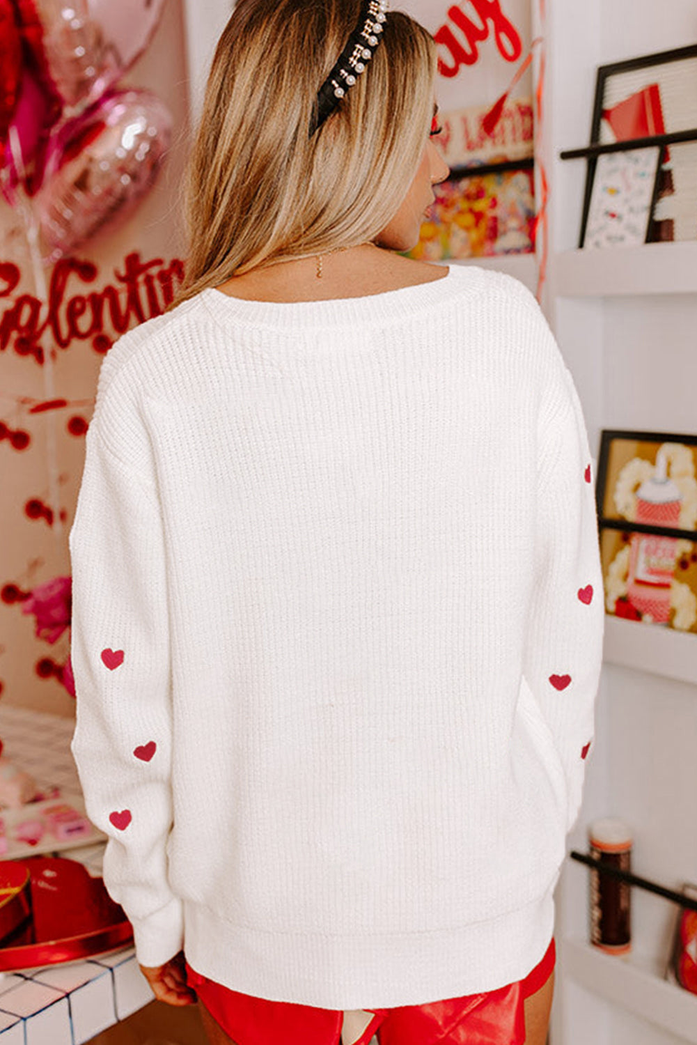 White ribbed crewneck sweater with embroidered red hearts on sleeves.