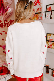 White ribbed crewneck sweater with embroidered red hearts on sleeves.