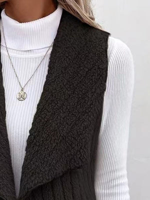 Black textured teddy collarless vest with waterfall lapel over white ribbed turtleneck.