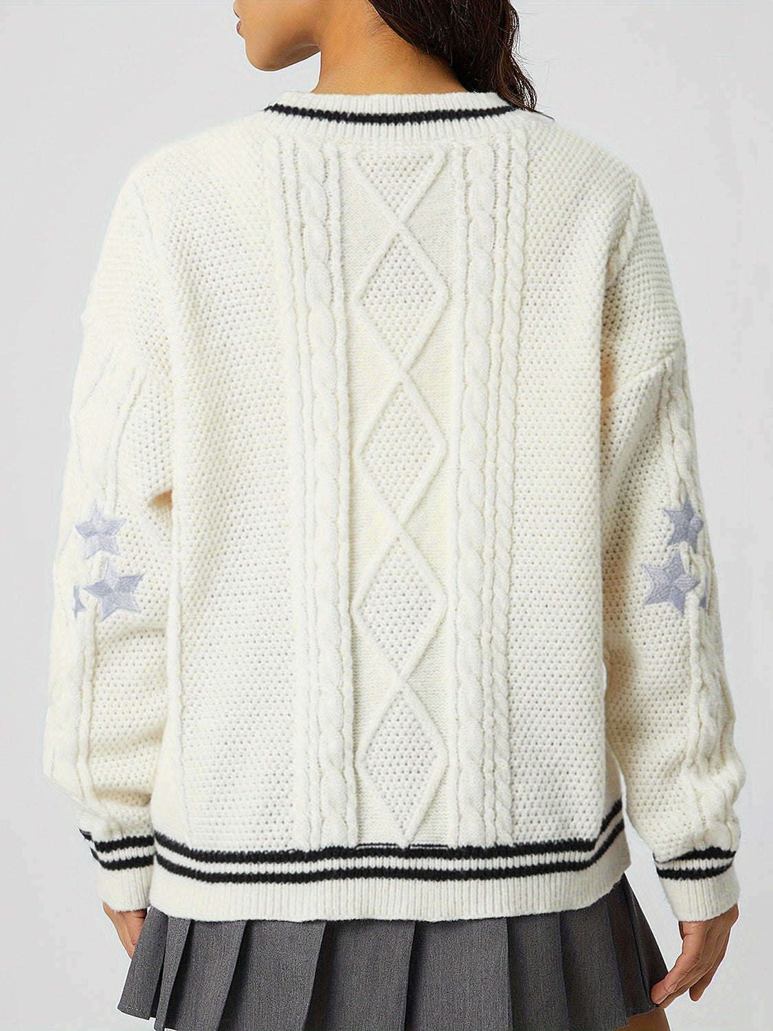White cable knit cardigan with diamond pattern, star details on sleeves, and striped trim.