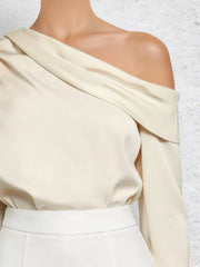Cream one-shoulder draped blouse with long sleeves and a chic, casual style.