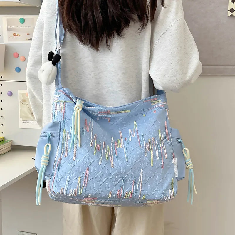 Light blue slouchy shoulder bag with embroidered colorful lines and diamond pattern.