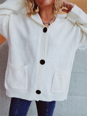 White chunky knit hooded button-down cardigan with pockets and dark buttons.