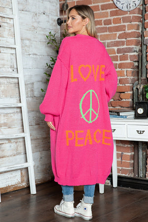 Pink knit maxi cardigan with "LOVE PEACE" and peace sign graphic, long sleeves.