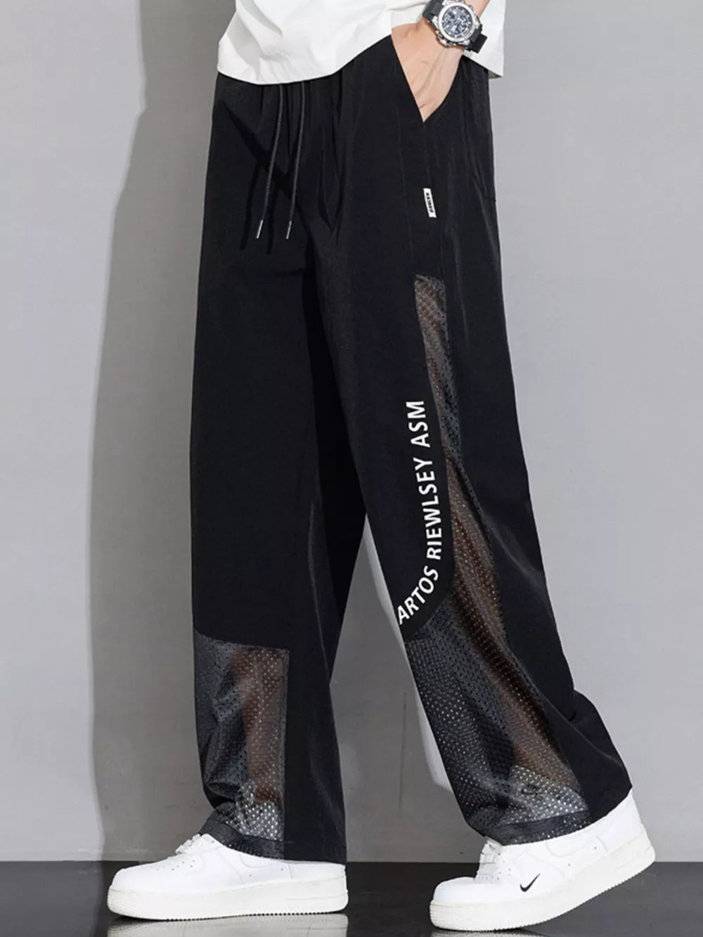 Black sweatpants with wide legs, mesh panels, and graphic text detail.