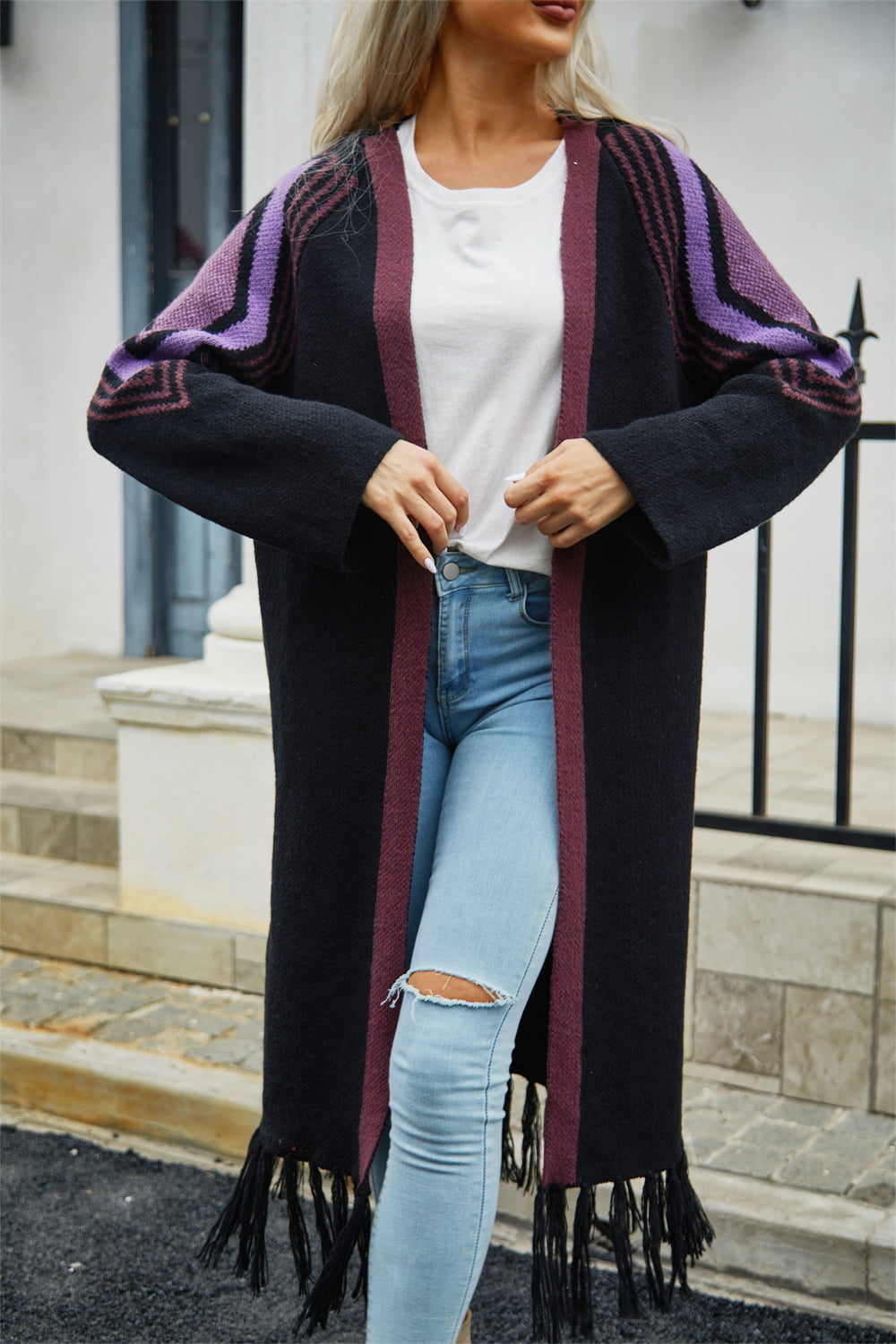 Black longline cardigan with geometric trim on sleeves and fringed hemline.
