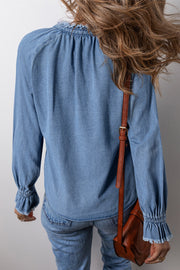 Light blue denim blouse with ruffled collar and cuffs, long sleeves, and a relaxed fit.