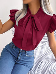 Burgundy pussy-bow blouse with ruffle sleeves and a tie neck, styled with jeans.