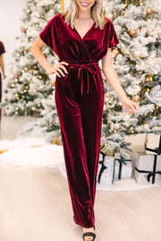 Burgundy velvet wrap bodice jumpsuit with tie waist and wide legs.