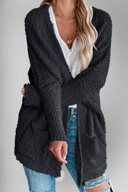 Black popcorn knit open cardigan with pockets, styled with a white v-neck top and jeans.