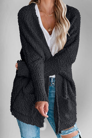 Black popcorn knit open cardigan with pockets, styled with a white v-neck top and jeans.