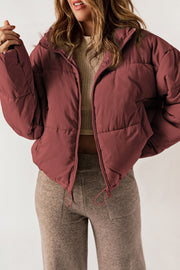Cropped puffer jacket in brick red with a hooded collar and zip closure.