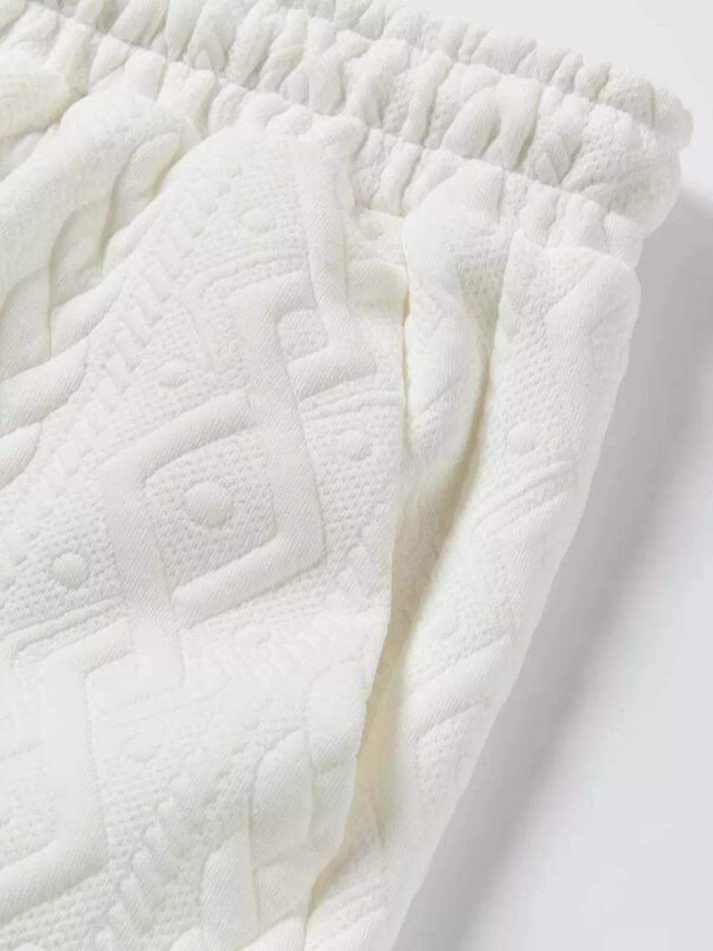 Off-white textured knit shorts with elastic waistband and geometric pattern detail.