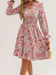 Romantic floral smocked dress in blush pink with v-neck, long ruffled sleeves, and tiered hem.