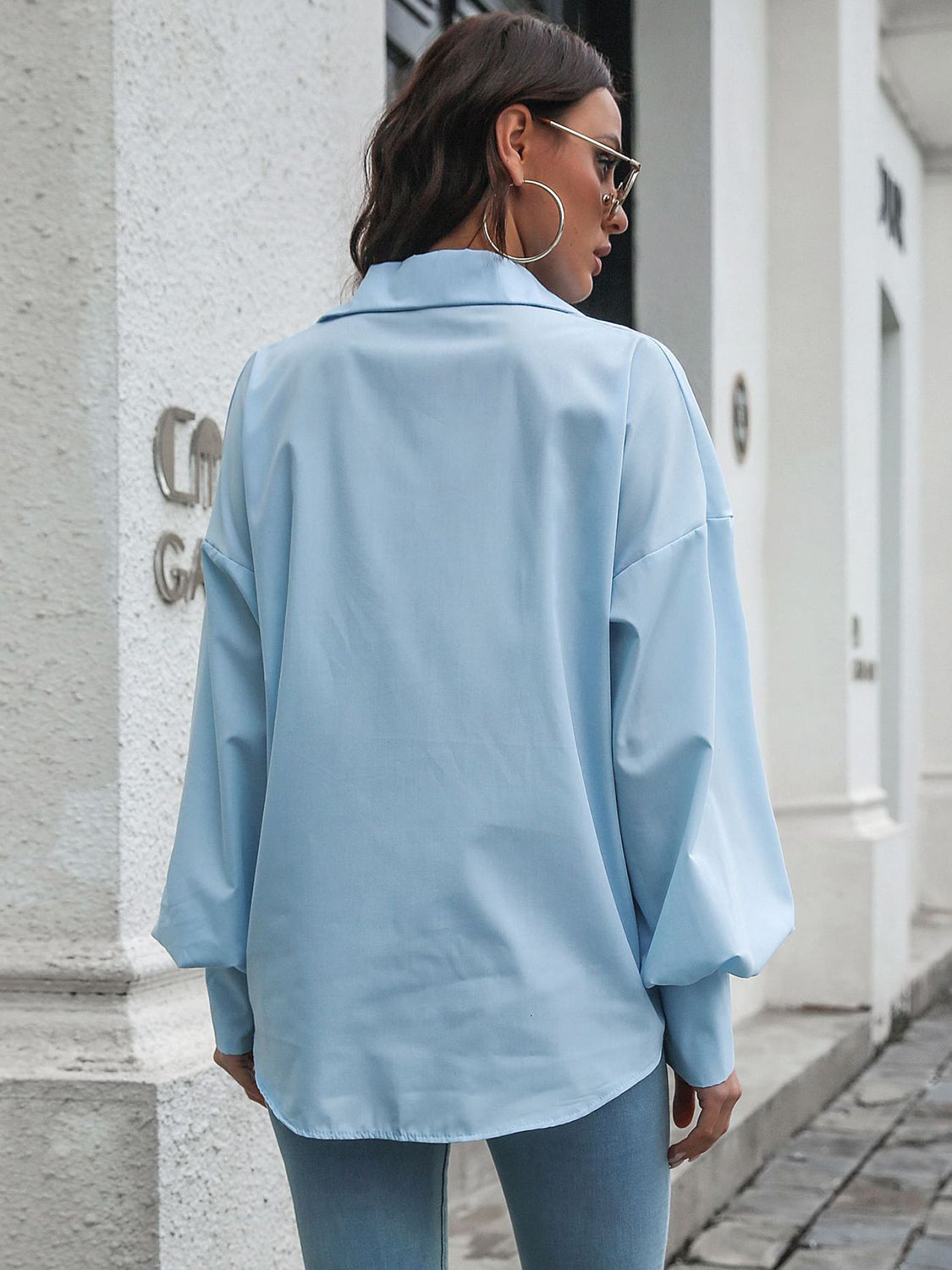 Blue oversized poplin blouse with blouson sleeves and buttoned cuffs.
