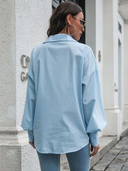 Blue oversized poplin blouse with blouson sleeves and buttoned cuffs.