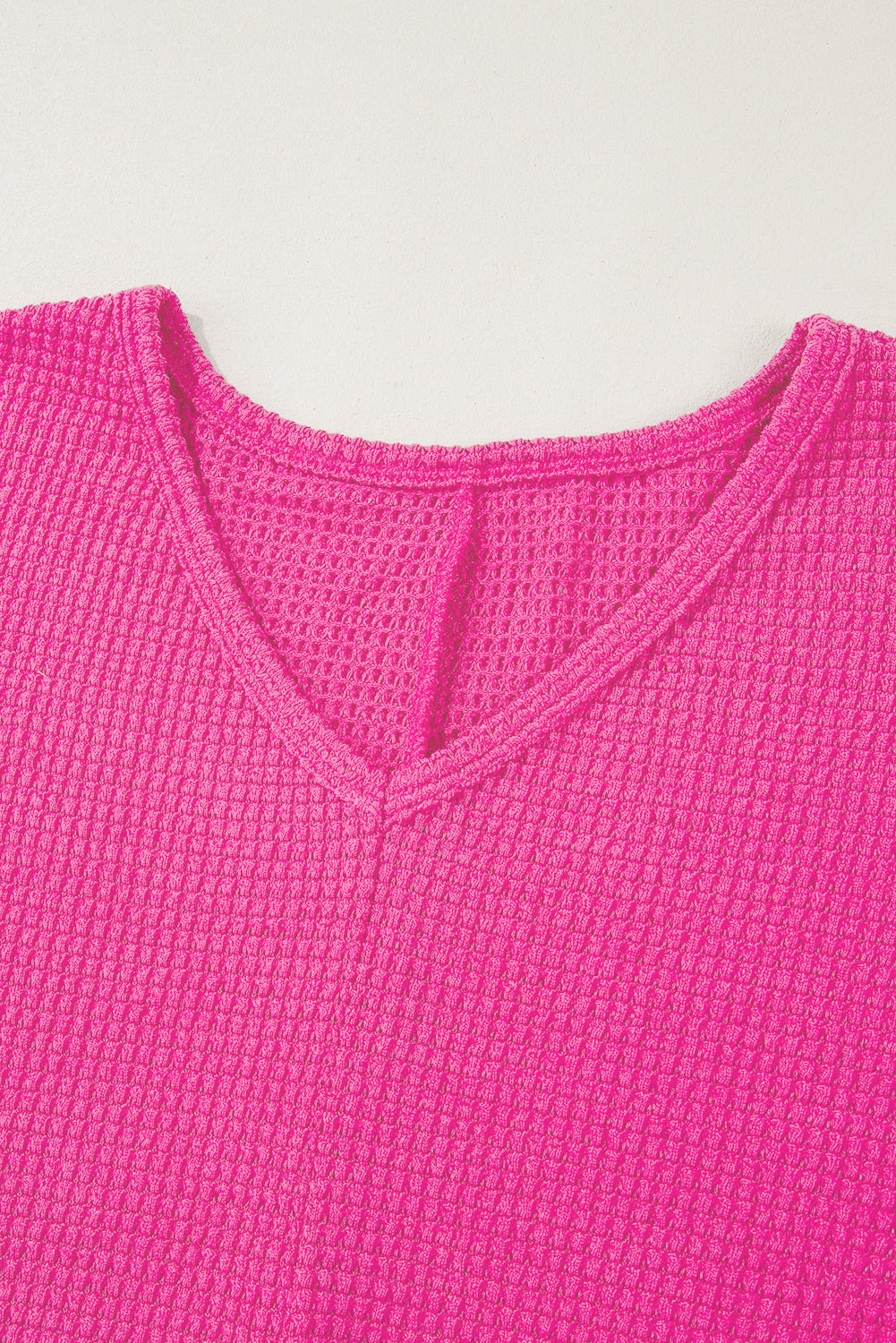 Hot pink waffle knit V-neck top with a slit hem detail.