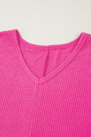 Hot pink waffle knit V-neck top with a slit hem detail.