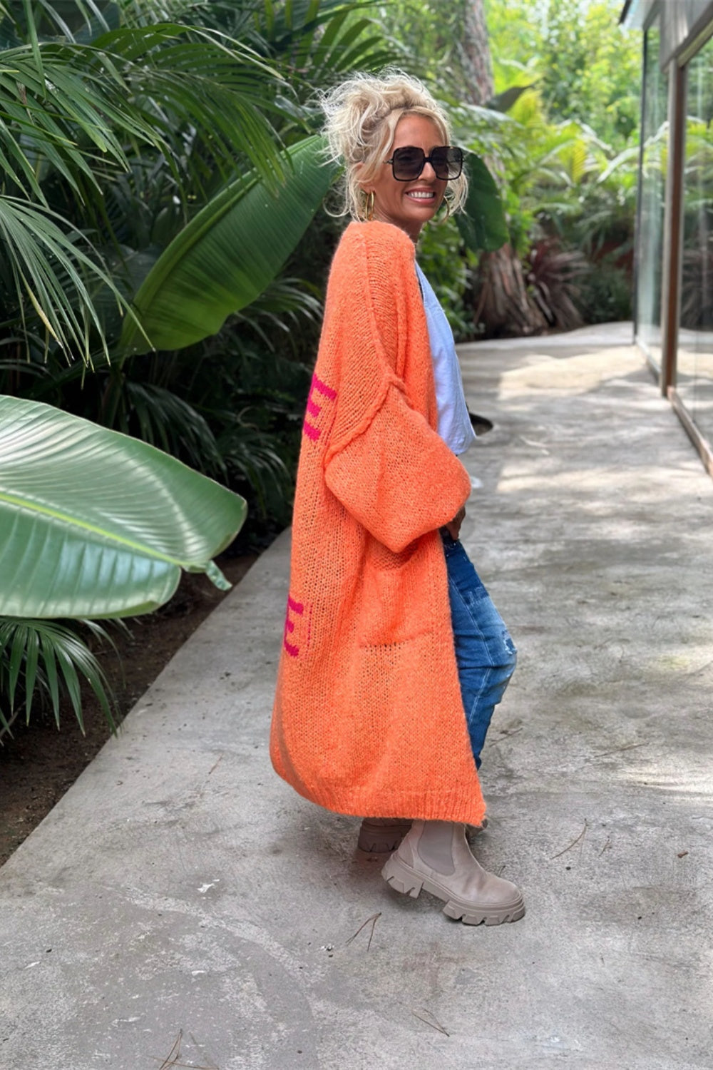 Orange maxi knit cardigan with pink peace sign detail and pockets, open front, long sleeves.