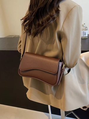 Sleek faux leather crossbody bag in coffee color with a wavy flap closure.