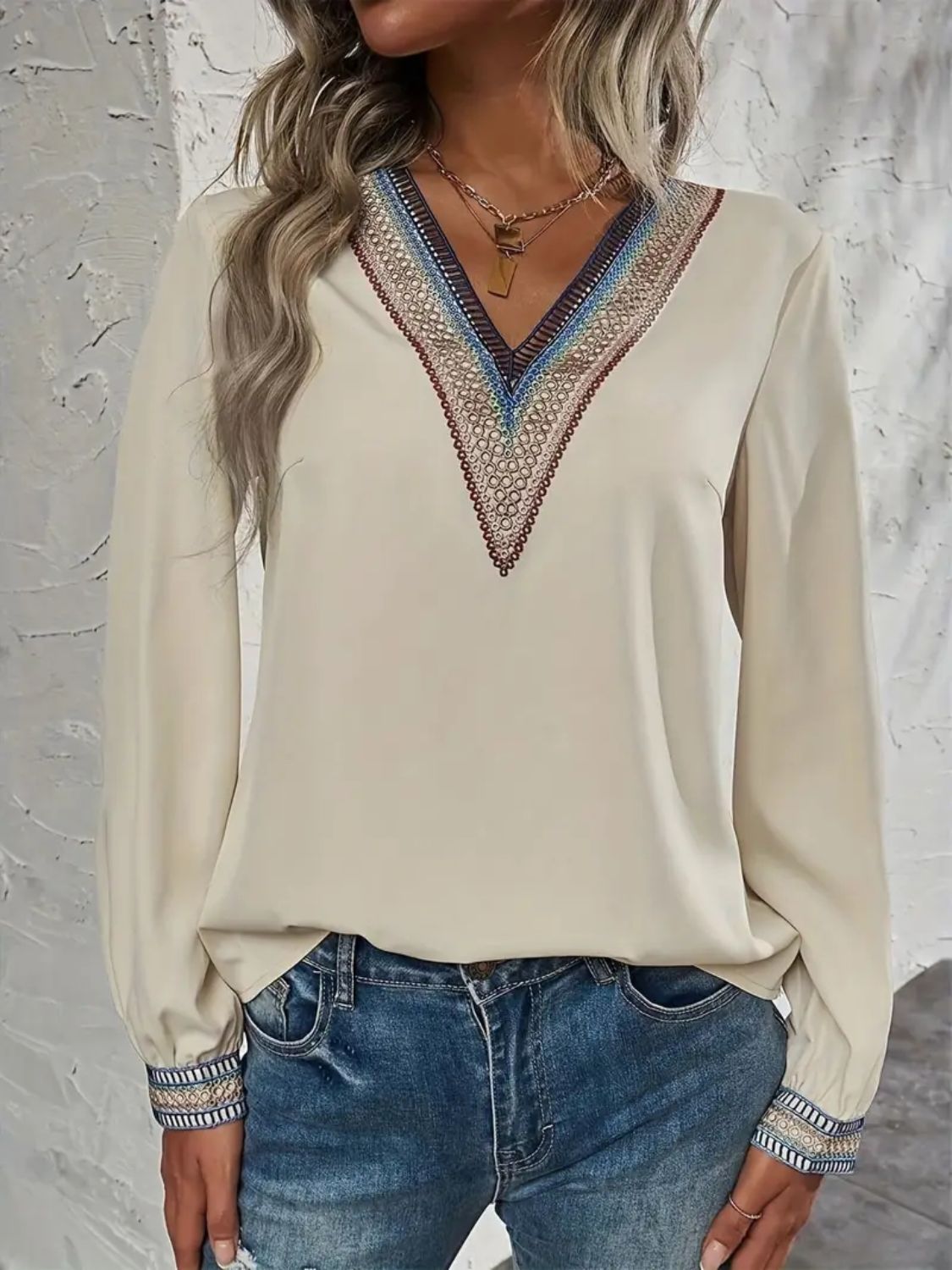 Beige V-neck blouse with colorful embroidered trim on neckline and cuffs.