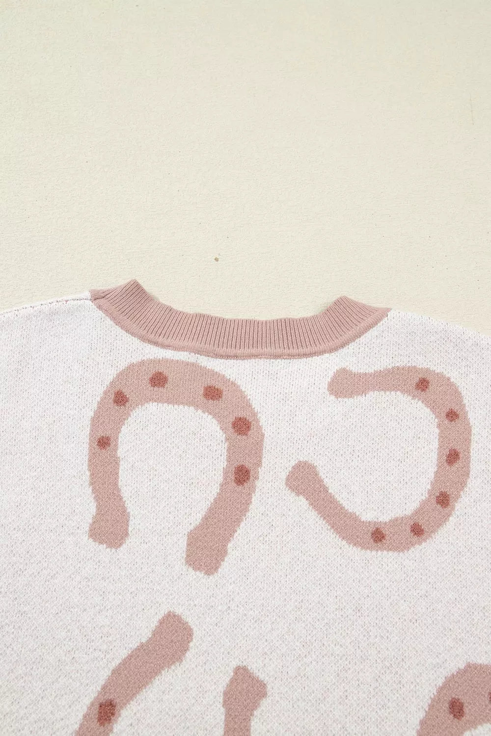 White knit top with pink horseshoe pattern and ribbed crew neck.