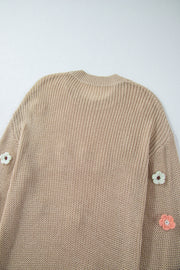 Khaki knit sweater with embroidered floral details on the sleeves.