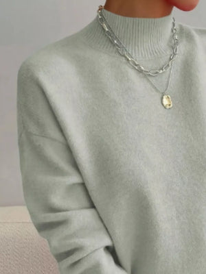 Light green mock neck sweater with dropped shoulders, styled with layered necklaces.